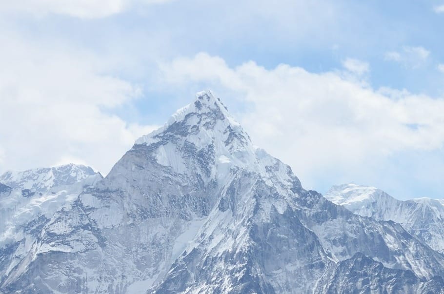 A mountain in daylight, with clouds around and a blue sky above.